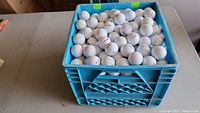 Plastic milk crate filled with approximately 350 white golf balls on a table