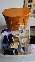 Closed oval wooden jewelry box and plastic bin with jewelry pieces arranged on table