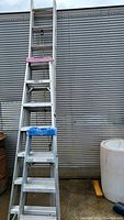Front view showing 4' and 7' step ladders and 10' extension ladder leaning against corrugated metal wall.