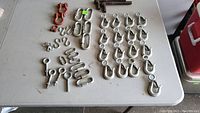 Full overview of all hardware pieces spread on table showing red shackles, silver hooks, carabiners and screw bolts.