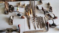 Wide view of all tools laid on table showing planes, brace drills, chisel handles, and bracing bits.
