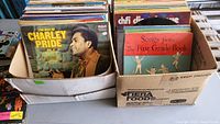 Two boxes of assorted vinyl records showing the front covers of albums 'The Best of Charley Pride Vol. II' and 'Songs from The First Grade Book'.