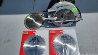 Fully visible Black & Decker circular saw with one blade mounted and two packaged saw blades underneath.