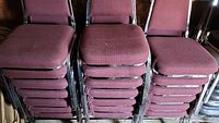Photo showing three stacks of seven burgundy fabric stackable chairs with chrome frames.