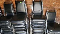 Side view of stacked black cushioned chairs with metal frames showing condition of the seats and legs.