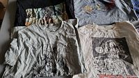 Top view of four T-shirts showing Marvel Avengers and other graphic prints in gray, black and light colors.
