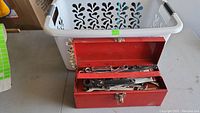 Red metal toolbox containing several metallic wrenches including combination and ratcheting types.