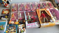 Wide shot showing assortment of dolls in original packaging including Spice Girls dolls, Barbie Real Life boxed dolls, Toy Story figures, and several McDonald's promotional booklets and toys.