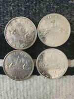 Top side view showing the four Canadian silver dollar coins with the Voyageur canoe design and year 1962, 1963, 1963, and 1965 visible.