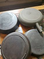 Underside of three cast iron skillets showing brand markings and condition
