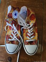 Front view of both Converse high top shoes featuring the pizza slice print on canvas uppers, white laces, and logo patches visible on the inside ankle.