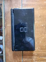 Closed view of black Nintendo DS handheld console showing exterior top lid with Nintendo DS logo and visible wear/scratches.