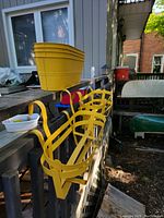 View of four yellow rectangular outdoor plant pots stacked and four yellow metal hanging brackets attached to a railing.