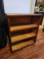 Front view of the pine bookshelf showing three shelves and visible wear on surfaces.