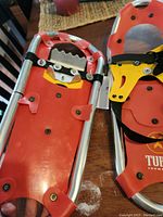 Close-up front view of one Tubbs snowshoe showing red decking, yellow bindings with black straps, and metal crampons.