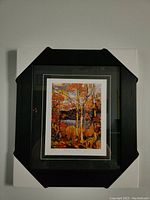 Front view of framed print wrapped with protective corner guards showing autumn landscape with birch trees in orange and yellow tones.