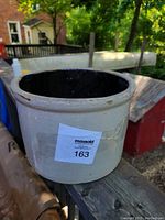 Side-angle photo of the beige stoneware crock with black glazed interior visible on an outdoor wooden surface.