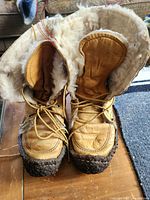 Front view of vintage tan leather snow boots with thick shearling lining and rugged rubber soles, laced up with leather laces.