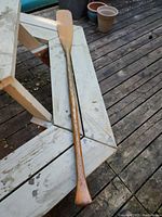 Full wooden paddle laid out on a white wooden bench, showing the entire length and handle.