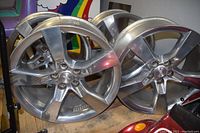 Front view of a silver 5-spoke alloy wheel leaning against two others