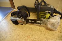 Photo showing Craftsman and Ryobi gasoline-powered chainsaws side by side on the floor.
