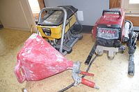Two portable paint sprayers on floor near wall. One red Titan Impact 440, one yellow Paint Crew 770. Both connected to hoses and paint spray guns with red handles.