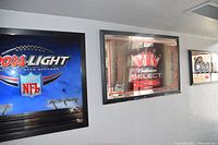 Three framed and mirrored beer signs mounted on a wall: Coors Light NFL, Budweiser Select neon, and Coors.