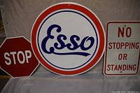 Three metal signs shown side by side: small red octagonal STOP sign, round Esso sign with blue cursive text and red border, rectangular white No Stopping Or Standing sign with red text.
