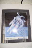 Framed color poster of astronaut in Manned Maneuvering Unit suit, floating against a backdrop of space and Earth, signed by Bruce McCandless II.
