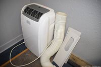Full view of Black & Decker portable air conditioner with attached white flexible exhaust hose and separate window slider panel leaning against the wall.