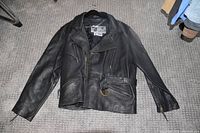 Full frontal view of the black leather motorcycle jacket showing zippered pockets, belt with metal buckle, and sleeve zippers.