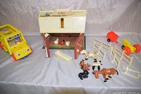 Photo shows wood and plastic Fisher Price barn with open doors and various farm animals in front alongside white fencing pieces and yellow tractor