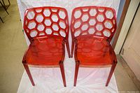 Two cherry red translucent plastic chairs with honeycomb pattern on backrests, side by side on white backdrop.