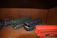 Metal vintage train cars in a wooden shelf, showing four cars in a row including a green car, black car with roof damage, and a red car.