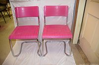 Frontal view of two pink plastic and chrome stacking chairs side by side, showing seat and back details.