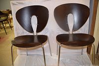 Front view of two dark wood and chrome metal stacking chairs side by side showing sculptural open backrests and curved seats.