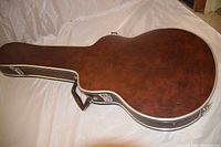 Brown guitar case laying closed horizontally, showing top side with handle and metal latches.