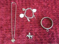 Necklace, charm bracelet and bangle bracelet displayed together on red textured fabric.