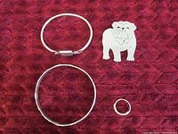 Four sterling silver jewelry pieces on red textured background - two bracelets, one bulldog pendant, one ring