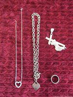 Overview photo showing two silver necklaces with pendants, one with open heart and one with solid heart pendant. Also visible is the simple ring and cross pendant with figure.