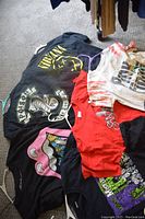 Photo shows a group of band and metal rock t-shirts laid out on carpet including Nirvana, Poison, Rolling Stones, tie-dye, and other designs