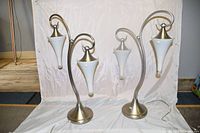 Pair of matching double-arm table lamps with brushed metal bases and frosted glass cone-shaped shades on white fabric background.