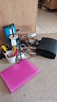 Overview of lot showing Amazon Echo box, desk lamp, portfolio, pink folder, flashlight, scissors, and cup with writing utensils.