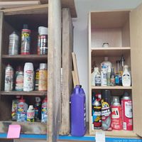 Wide view of wooden shelving units storing various automotive detailing and maintenance products including spray paint, degreasers, brake fluid, and Flex Seal liquid rubber sealant (purple bottle).