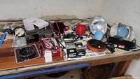 Wide view of automotive parts on workbench including lighting fixtures, battery charger, distributor cap, and packaged components