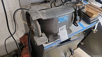 Full side view of the bench grinder showing grinding wheel, metal body, and power cord.