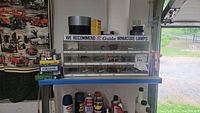 Wide shot showing Guide miniature lamps in plastic organizer case, various tape rolls on top, and spray cans below shelf.