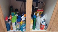 Multiple cleaning products stored in a cupboard, various spray bottles and liquids visible