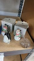 Two Fenton art glass snowmen figurines with original boxes and clear glass snowflake paperweight on shelf.