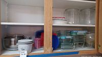 Wide view showing shelves with multiple glass food storage containers with lids, a few stainless steel bowls, and some ceramic containers with lids.
